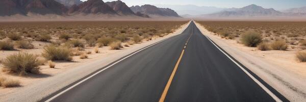 An empty road in the desert with mountains in the background photo