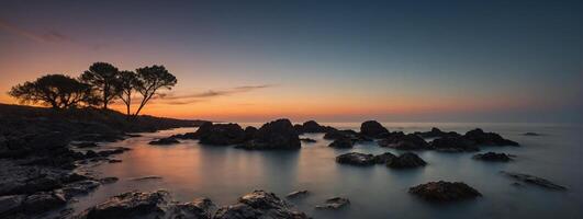 A beautiful sunset over the ocean with rocks and trees photo