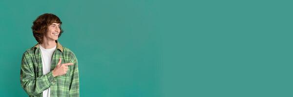 Cool stylish guy with curly hair pointing aside on color studio background, copy space for design, panorama photo