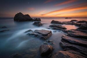 A long exposure photograph of rocks and water at sunset photo