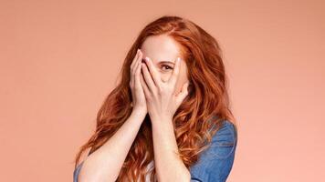 A woman is sitting with her hands covering her face, blocking her eyes. She appears to be playful, isolated on colorful background photo