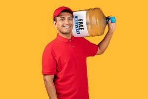 A cheerful delivery worker in a red uniform and cap is holding a large water jug on his shoulder. The worker appears friendly and approachable against a vibrant yellow background. photo
