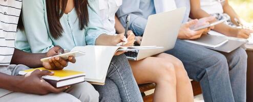 Diverse students studying outdoors in campus with books and devices, preparing for exams, cropped image, closeup photo
