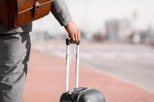 Unrecognizable businessman is walking with his luggage outside a modern airport. The mood is dynamic and professional, highlighting travel and business with a sleek airport backdrop. photo
