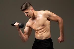 A man is lifting a dumbbell in front of a plain gray background. He is focused and determined, showcasing strength and fitness. photo