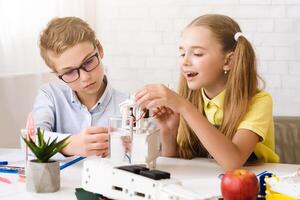 Two students, a boy and a girl, work together on a science project in a classroom setting. The boy is wearing glasses and is focused on robot photo