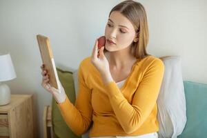 A girl is seated on a bed, gazing at her reflection in a mirror placed in front of her. She appears contemplative as she studies her own features in the reflective surface. photo
