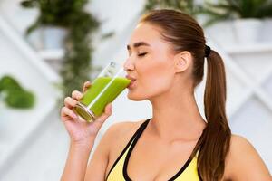 A woman drinks a refreshing green smoothie, enjoying a healthy and refreshing beverage in a bright, modern gym setting. photo