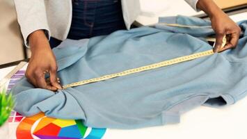 African American woman measuring a shirt using a tape measure. The individual is carefully extending the tape measure along the length and width of the cloth to determine its dimensions accurately. photo