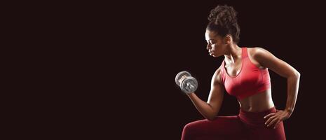 African woman bodybuilder doing workout with dumbbells, single arm db curl, side view, black studio background photo