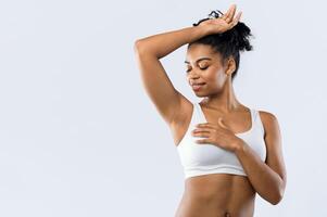 Happy afro woman smelling her fresh armpit over grey background, putting hand up, copy space, advertisement for under arm deodorant photo