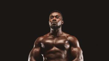 A muscular man stands against a black background, looking upwards with a determined expression. photo