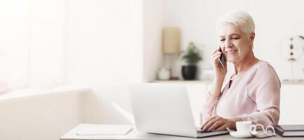Senior business woman working from home, discussing project with client, using laptop, panorama with empty space photo