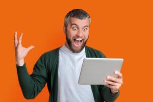 A man is holding a tablet in his hand and making a humorous expression on his face. He appears to be joking or reacting to something amusing on the device. photo