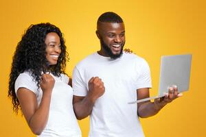 A couple, a man and a woman, both smiling and raising their fists in celebration while looking at a laptop. photo