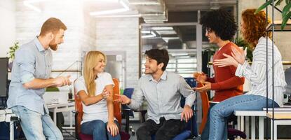 In the office setting, a diverse group of coworkers are seated closely together, engaged in a meeting or discussion, actively converse, gesturing and looking at each other while seated around a table. photo