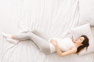 A pregnant woman is reclining on a bed surrounded by soft pillows. She appears comfortable and supported as she rests, top view, copy space photo