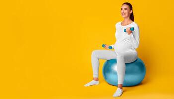 Pregnant Girl Exercising With Dumbbells Sitting On Fitball Over Pink Studio Background. Workout In Pregnancy. Copy Space photo