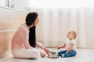 A woman is seated on the floor beside a baby, engaging in a close interaction. The woman appears attentive to the baby needs, providing care and support in a nurturing manner. photo