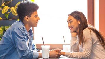 un joven negro chico y niña son sentado a un mesa en un cafetería, comprometido en conversación. ellos Aparecer relajado y contenido en su alrededores. foto