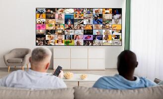 Two people are sitting on a couch in a living room, watching a large television screen displaying a multitude of smaller screens. They appear to be engrossed in the content displayed on the television photo