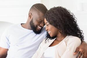 A close-up shot of a couple smiling and looking at each other while sitting on a couch. photo