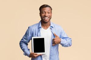 Cheerful Afro Man Showing Empty Tablet Screen Gesturing Thumbs Up Smiling At Camera Standing Over Yellow Background. Mockup, Studio Shot photo