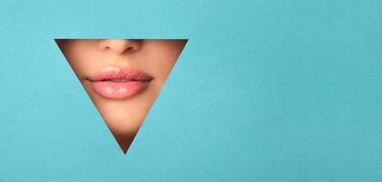 A woman face is visible through a geometric cutout in the shape of a triangle. She is looking directly at the camera, with one eye partially covered. The background is a simple, blank surface. photo