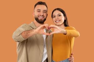 A man and woman are standing close together, forming a heart shape with their hands in front of their chests. They are smiling and looking at each other with joy. photo