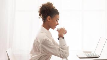 African American woman is sitting in front of a modern laptop computer, focused on the screen as she types and clicks. She appears to be working or studying intently in a home or office setting. photo