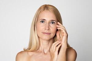 This image shows a portrait of a blonde woman with blue eyes. She is wearing no makeup and her skin appears to be naturally flawless. The woman is looking directly at the camera photo