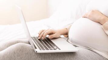 A woman is lying on a bed, engrossed in using a laptop computer. She is focused on the screen, typing and scrolling. The room is dimly lit, and she appears comfortable and relaxed. photo