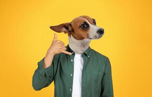 A dog with a human body is wearing a green shirt and a white undershirt. The dog has brown fur and white fur on its chest and face. The dog is making the call me gesture with its hand photo