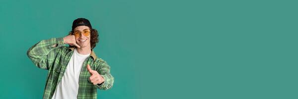 Portrait of confident curly teenager pointing at you and gesturing CALL ME on turquoise background, panorama with copy space photo
