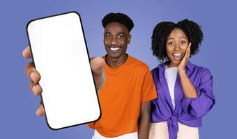 African American man and woman are standing side by side in front of a blue background. The man is holding out a smartphone with a blank screen towards the viewer photo