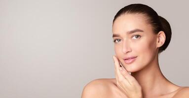 A woman is standing in a pose with her hand resting on her face. She looks directly at the camera with a neutral expression, showcasing a sense of contemplation, empty space photo