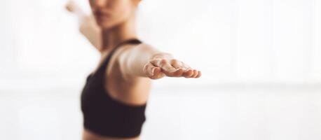 A person is practicing yoga inside a bright, airy space. The individual is in a focused stance, stretching their arms outward, which indicates they are engaging in a balancing pose, copy space photo