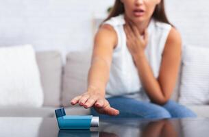Girl Reaching For Asthma Inhaler Preventing Respiratory Depression Sitting On Couch At Home. Shallow Depth, Selective Focus photo