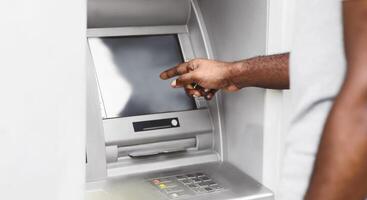 A close-up of a persons hand interacting with an ATM screen. The persons arm and shoulder are visible in the background. photo
