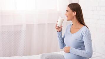 Happy Pregnant Lady Drinking Milk Sitting On Bed At Home. Empty Space For Text photo