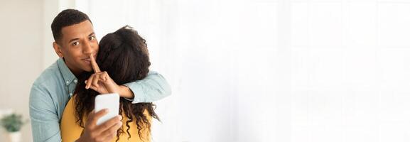 Loving african american couple hugging tightly, expressing love and affection, man using phone, with copy space for web-banner design photo