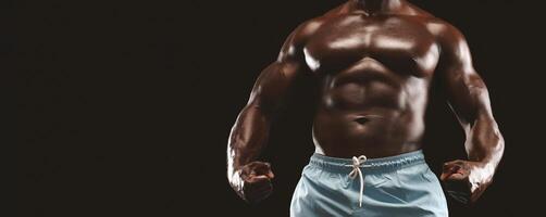 A muscular man with a toned physique poses with clenched fists in front of a black background. He is wearing blue shorts and appears to be in excellent shape. photo