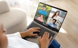 Black lady is engaged in a virtual meeting with four friends, visible on a laptop screen, in a bright and cozy room. Each participant is smiling, suggesting a joyful and interactive session. photo