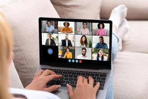 A person participates in a virtual team meeting on a laptop, engaging with multiple colleagues in a relaxed indoor setting, communicating for a work-related discussion. photo