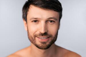 A close-up portrait of a man with short brown hair and a beard, smiling and looking directly at the camera. photo