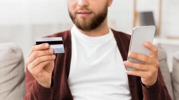A man holding a smart phone and a credit card in his hands, showcasing the action of making a digital payment transaction. The mans face is focused and intent on the screen of the phone photo