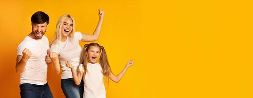 A joyful family of three is celebrating together, showing excitement through their enthusiastic gestures and happy expressions. The bright yellow background enhances the vibrant atmosphere photo