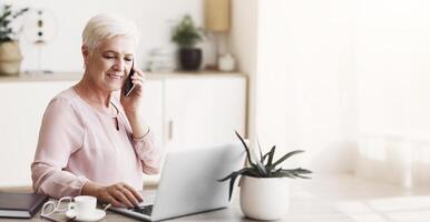 Senior business woman working in front of laptop, discussing project with client by cellphone, empty space photo