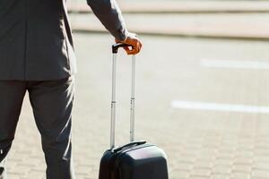 Unrecognizable businessman is standing with his luggage outside a modern airport. The mood is dynamic and professional, highlighting travel and business with a sleek airport backdrop. photo