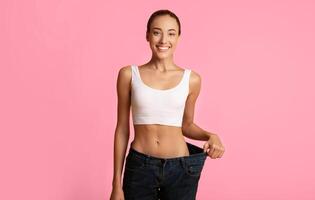 Weight Loss Concept. Slim Girl In Oversize Jeans Standing On Yellow Studio Background. Copy Space photo